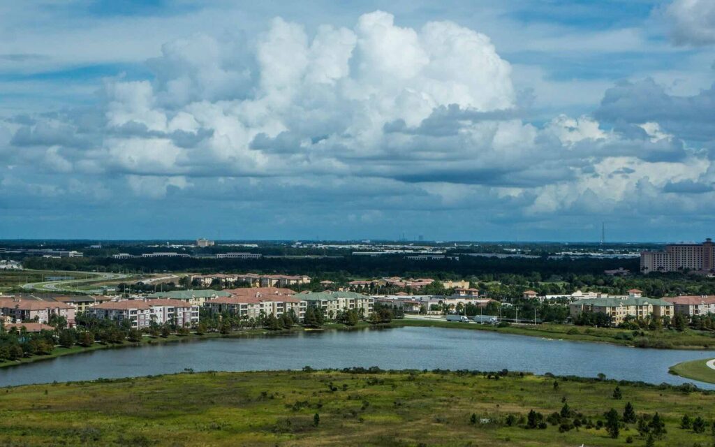 Aerial view of suburban Orlando, Florida area with calm lake in foreground, surrounded by residential buildings and lush greenery under cloudy sky - FAS Exteriors